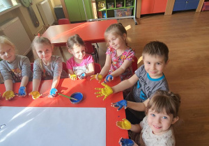 Dłonie dzieci zostały pomalowane farbą w kolorach żółtym i niebieskim.